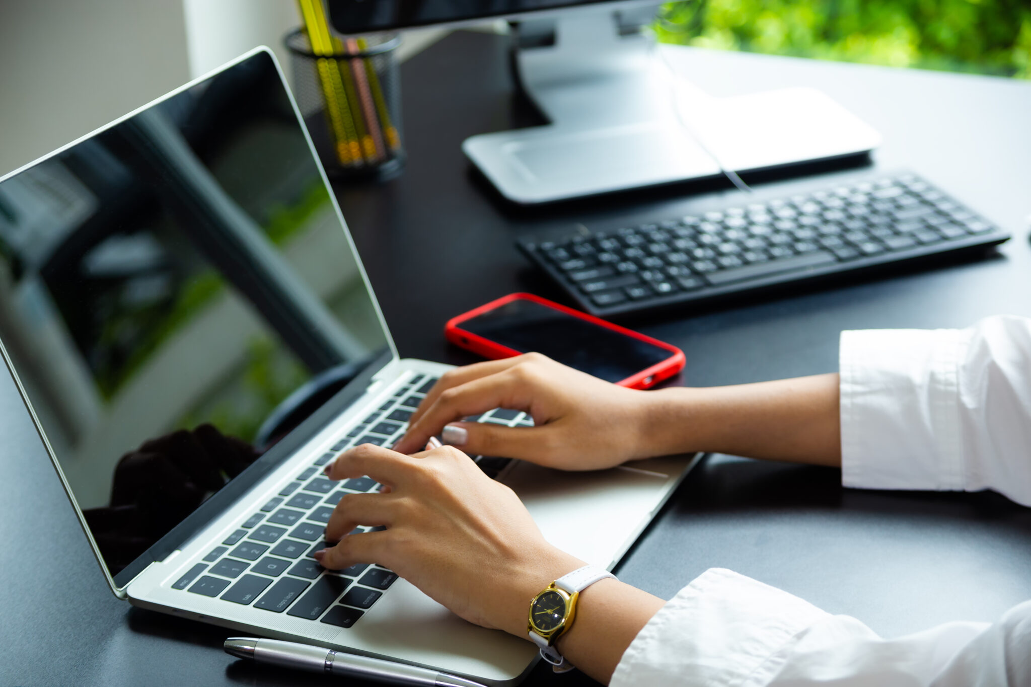 Close up hand of female typing on keyboard of laptop on table, working with technology device in modern office